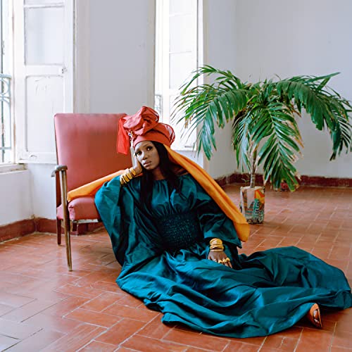 Woman in teal and orange clothing seated on a tiled floor.