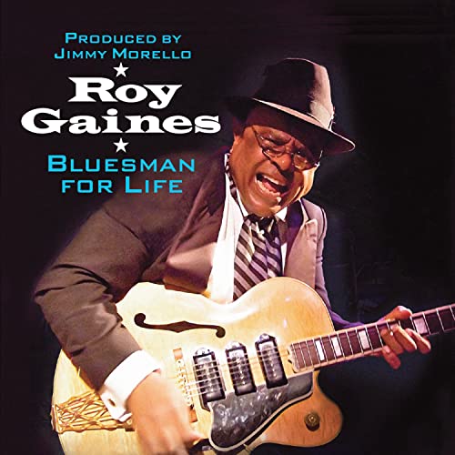 Roy Gaines, a blues musician with a guitar, smiles while performing.