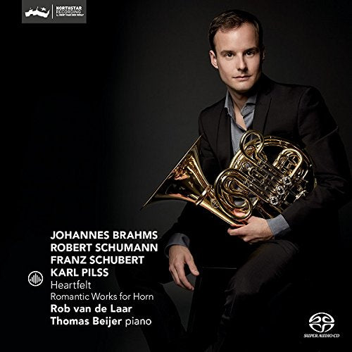 Man in a black suit holding a French horn, against a dark background.