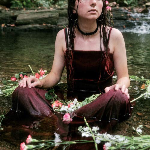 Woman with wet hair and flowers, seated in shallow water.