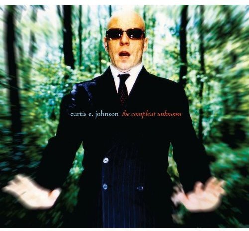 "Album cover featuring a bald man in a suit, standing in a forest."