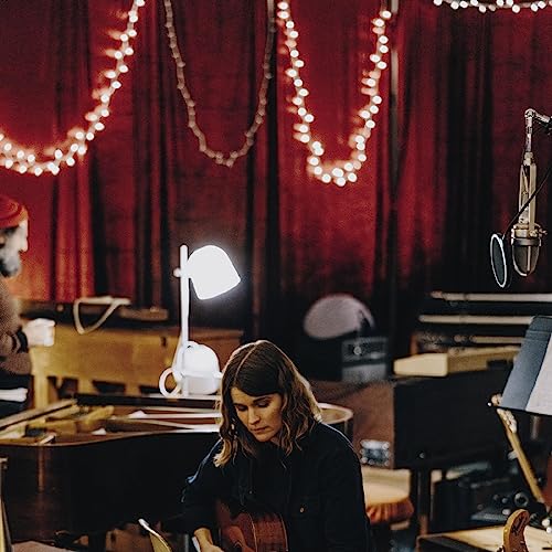 Woman playing guitar in a room with red curtains and lights.