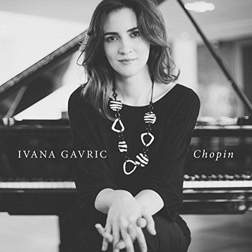 Black and white image of a woman sitting by a piano, wearing a dark dress.