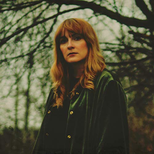 Woman with long, wavy auburn hair wearing a dark jacket.
