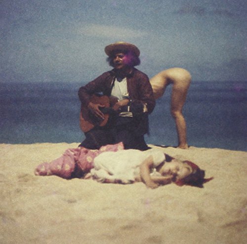 A man plays guitar beside a reclining woman on a sandy beach.