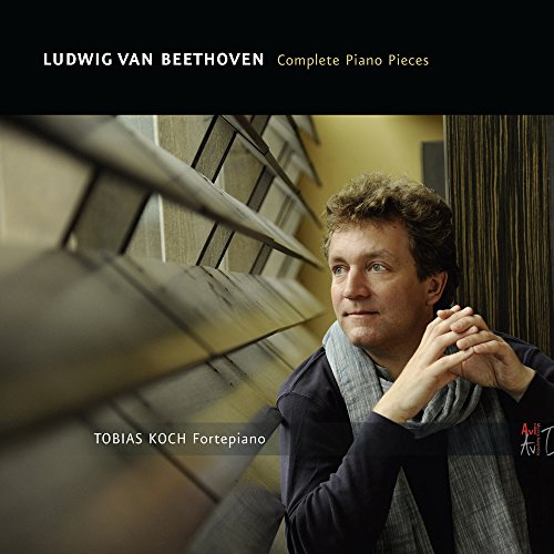 A man in a dark jacket and scarf sits beside a piano, looking thoughtful.