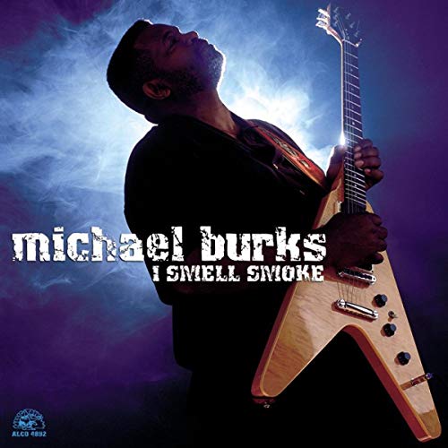 Michael Burks plays a V-shaped guitar against a purple smoky background.