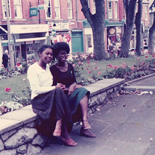 Two Black women sitting together on a stone ledge in a city setting.