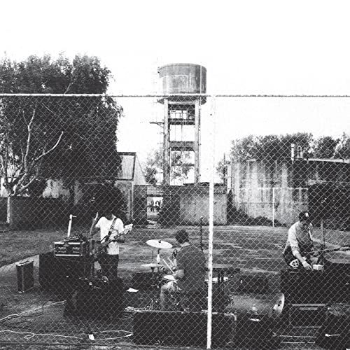 Black and white photo of a band playing behind a chain-link fence.