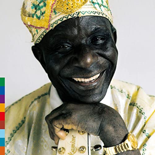 Smiling older Black man with a patterned cap holding a guitar.