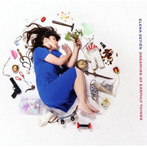Woman in blue dress surrounded by objects on a white background, album cover.