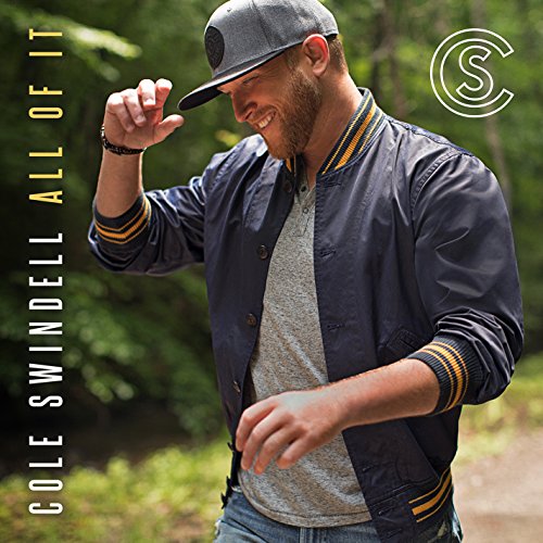 Cole Swindell wearing a baseball cap and varsity jacket in a wooded setting.