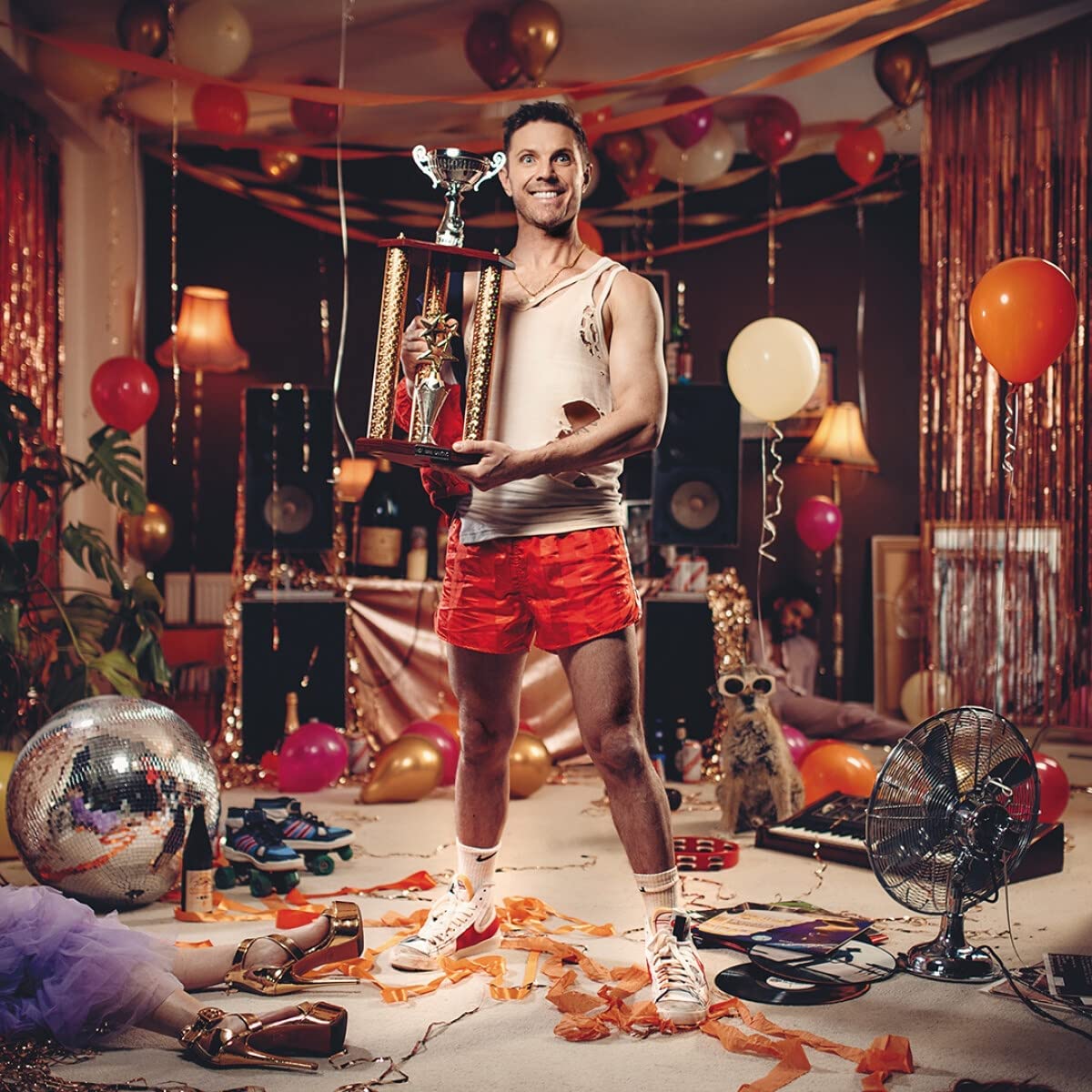 Man holding trophy in a room decorated with balloons and party decorations.
