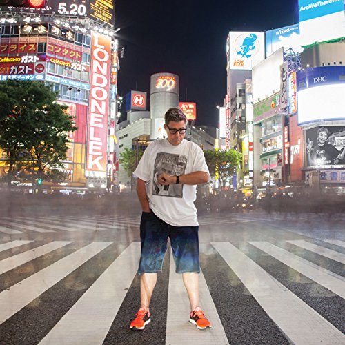 A man stands on a crosswalk at night, surrounded by bright city lights.