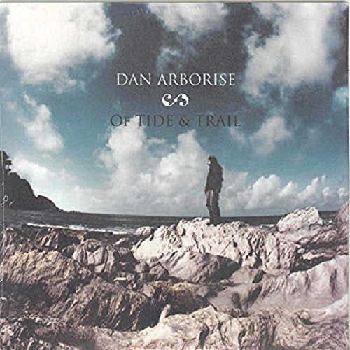 "Album cover with a man standing on a rocky shore under a cloudy sky."