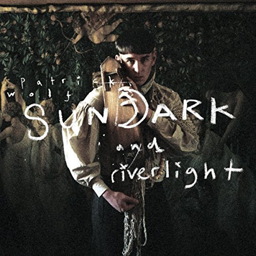 "Album cover featuring a man holding a cello, surrounded by foliage and statues."