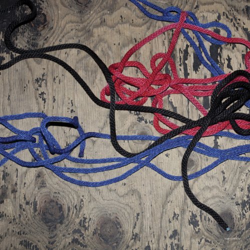 Tangled red, blue, and black cords on a grey wooden surface with visible knots.