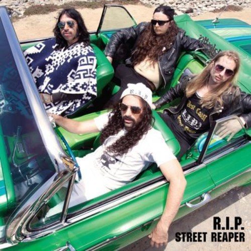 Four people in sunglasses pose in a classic green convertible car.