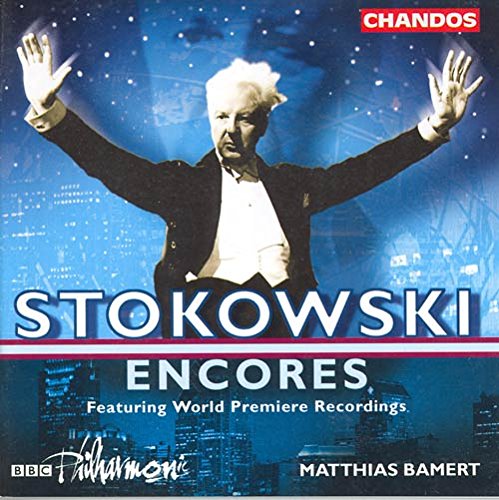 Conductor in a tuxedo with raised arms against a blue cityscape background.