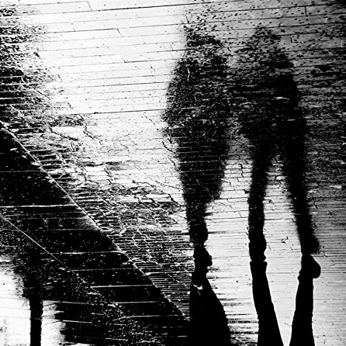 Black and white photo of a person’s blurred reflection on wet pavement.