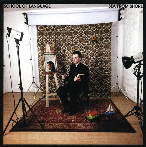 Man with painting and studio lights on patterned backdrop.