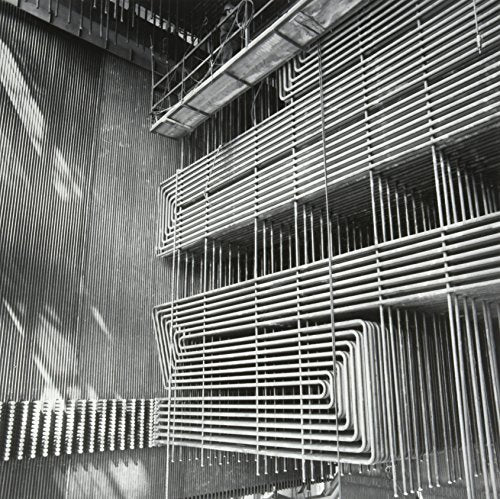 The alt text for the image is: "Black and white photo of industrial pipes and metal grating."