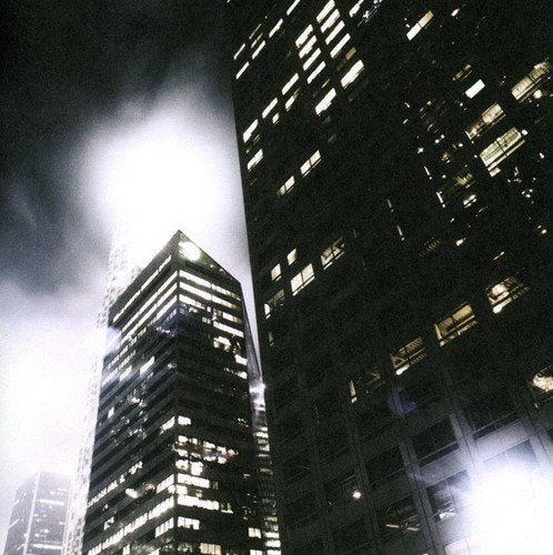 Dark, low-angle view of illuminated skyscrapers partially obscured by fog.
