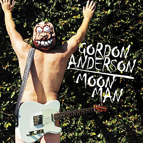 Person with a grotesque mask holding a guitar in foliage.