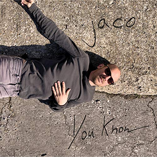Man lying on cracked pavement, wearing dark clothing and sunglasses, with 'Jaco You Know' written.