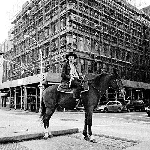 Black and white photo of a cowboy on horseback in a city street.
