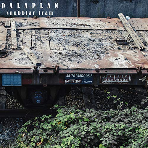 Rusty freight car with lettering and overgrown vegetation nearby.