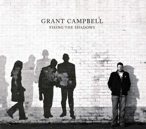 "Album cover with man standing by a brick wall and shadowy silhouettes."