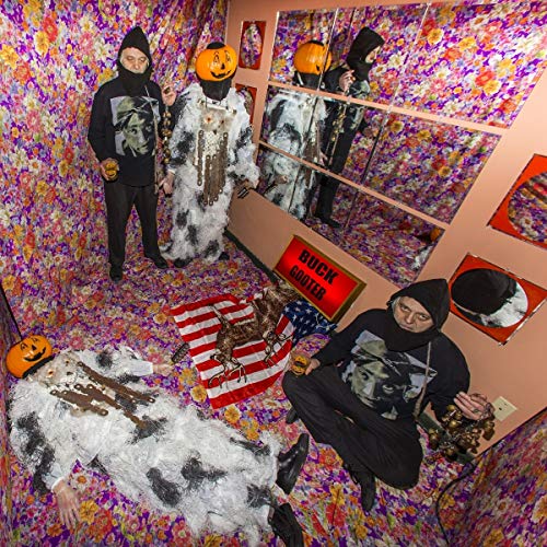 Three people in black hoodies and one in a white costume in a colorful room.