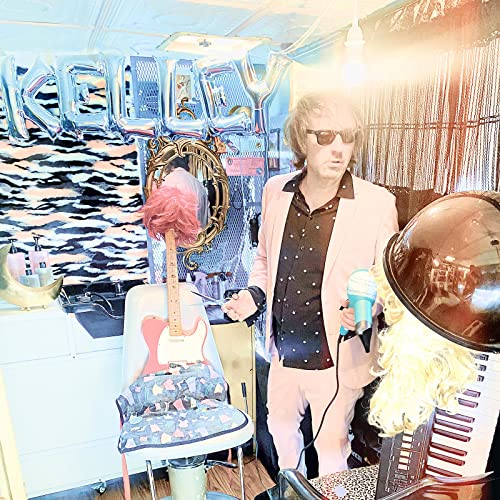 Man in pink suit standing in a brightly decorated hair salon.