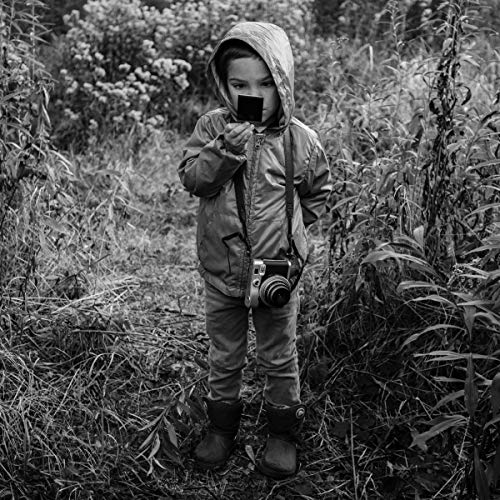 Black and white photo of a child with a camera in a field.