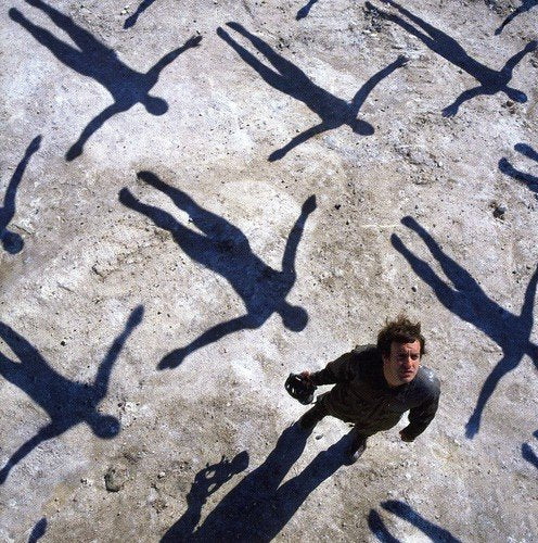 A man surrounded by his shadow and multiple other shadows on a grey surface.