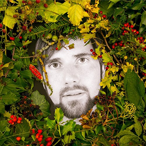 Black and white portrait of a man surrounded by green foliage and berries.