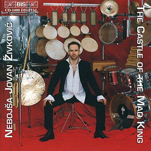 Man seated amongst various percussion instruments on a red background.