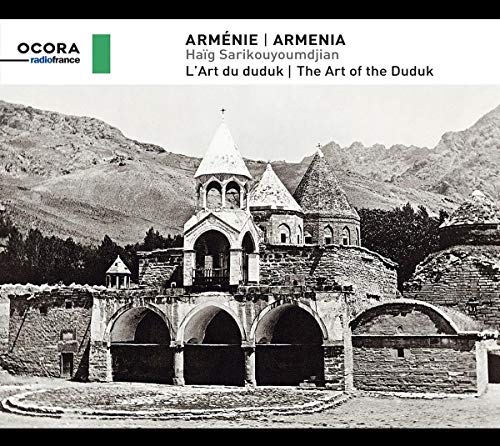 "Black and white image of a stone church with mountains in the background."