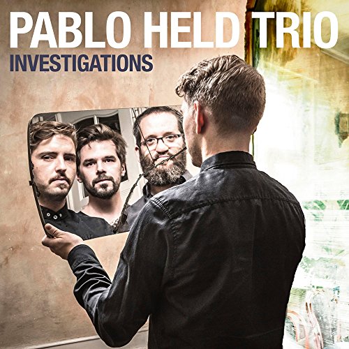 Man holding a tablet showing three men's faces, Pablo Held Trio album cover.