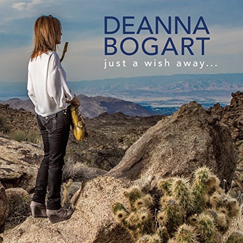 Woman standing on rocky cliff, holding guitar, with desert landscape in the background.
