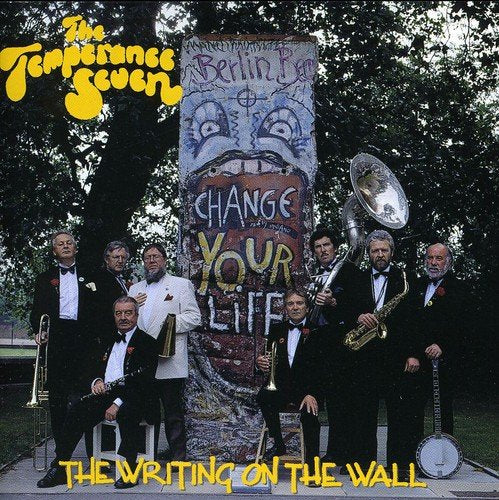 "Album cover featuring seven suited men with instruments beside a graffiti-covered concrete pillar."