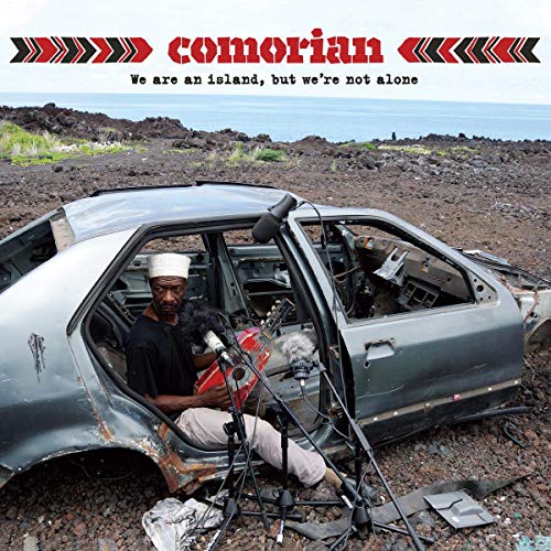 "Album cover with a man sitting in a wrecked car holding a microphone."