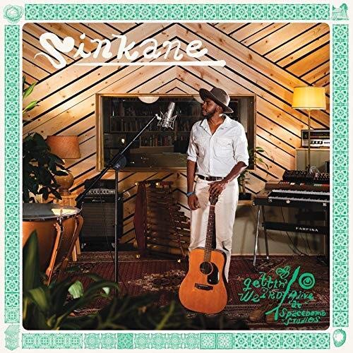 Sinkane stands with a guitar in a wood-paneled recording studio.