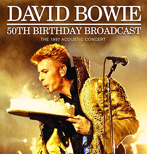 David Bowie holding a birthday cake with candles, concert background.
