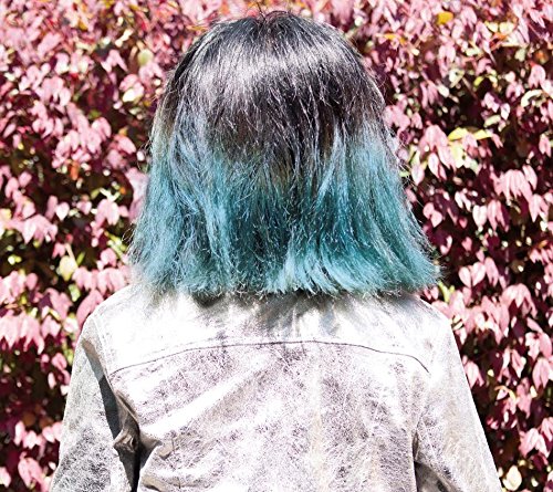 Woman with teal and silver hair seen from behind, pink foliage.