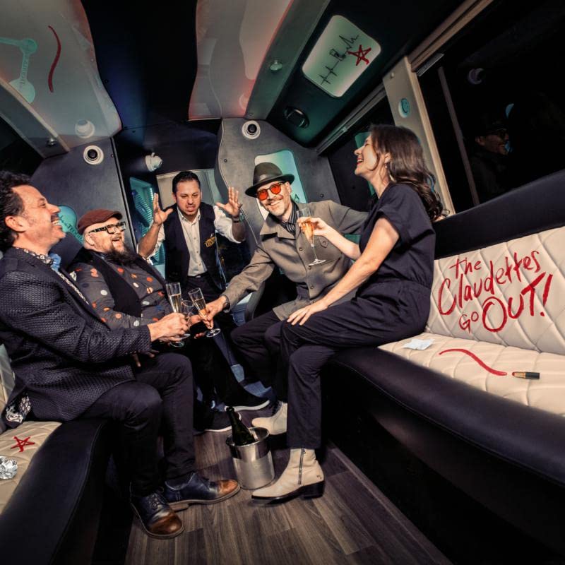 Band members inside a limousine, holding drinks and smiling.