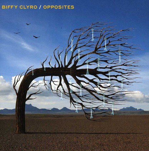 "Bare tree with icicles in a desert landscape, blue sky and mountains in background."