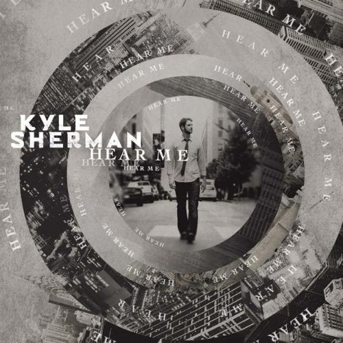 Album cover with man standing, surrounded by cityscape and "Hear Me" text in spiral pattern.