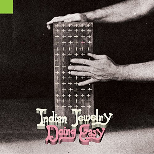 "Black and white image of hands holding a grid-patterned vinyl record cover with pink and white text."
